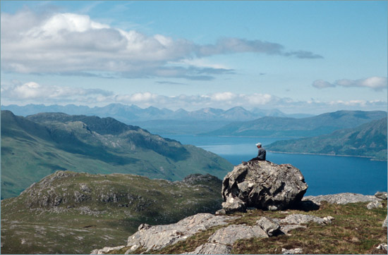 Mieke on a rock at An Caisteal's rim; in the distance: the mountains of Skye