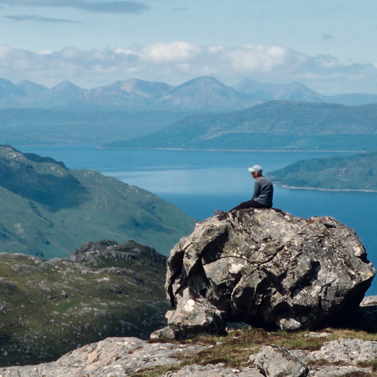 Zoom: Mieke on a rock at An Caisteal's rim; in the distance: the mountains of Skye