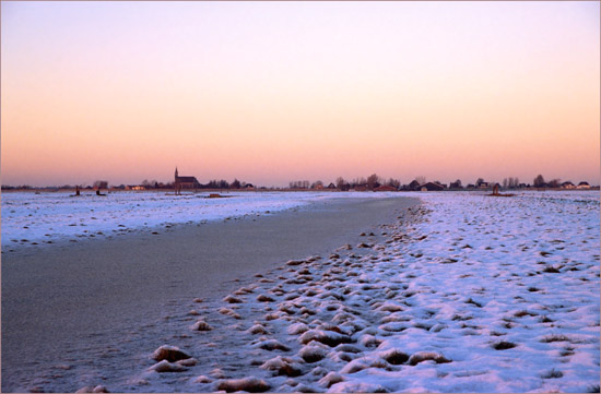 Bevroren land in de Beetskoog bij zonsondergang, met Oudendijk op de achtergrond