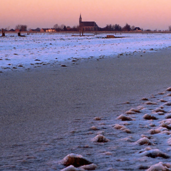 Zoom: Bevroren land in de Beetskoog bij zonsondergang, met Oudendijk op de achtergrond